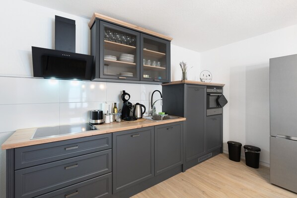 Una cocina moderna con armarios grises, microondas integrado, cafetera y refrigerador de acero inoxidable.