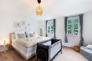 Une chambre à coucher comprenant un lit, un berceau, une fenêtre avec des rideaux, une lampe de chevet et un luminaire fixé au mur.