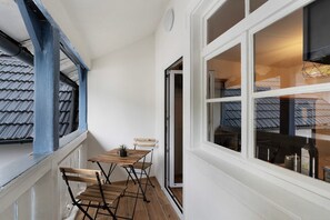 A room with a wooden table, chairs, a small potted plant, and a window with a view of a building.