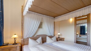 A bedroom with a wooden headboard, two beds, a nightstand with a lamp, a mirror, and a wall-mounted light.