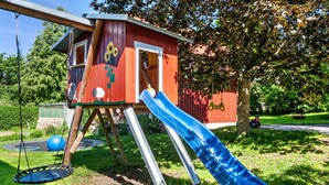Una casita de juegos de madera con un tobogán, un columpio y un trampolín.