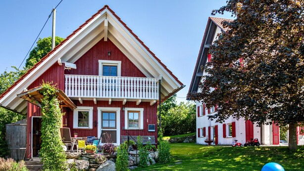 Una casa roja con balcón, jardín y un trampolín.