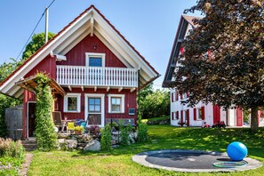 Ett rött hus med en balkong, en trädgård och en studsmatta.