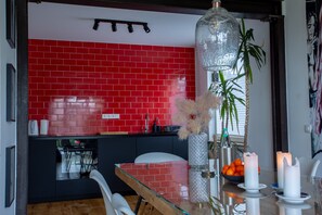Une cuisine moderne avec des carreaux rouges, une table à manger en verre et un luminaire suspendu.