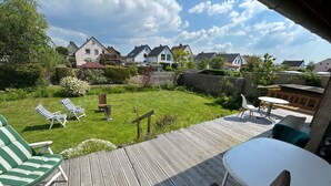 Een terras met buitenmeubilair, een gazon en huizen op de achtergrond.