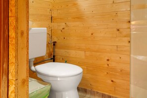 Un baño con paneles de madera, un inodoro blanco y una tubería de fontanería visible.