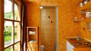 A wooden interior with a kitchen, a toilet, and a window with curtains.