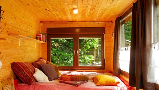 A wooden cabin room with a bed, a window, and a door.