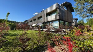 A modern building with a sloped roof, large windows, and a garden with red berries. - Exclusive 5-room maisonette architect's house with panoramic lake view and penthouse roof terrace (Öhningen)