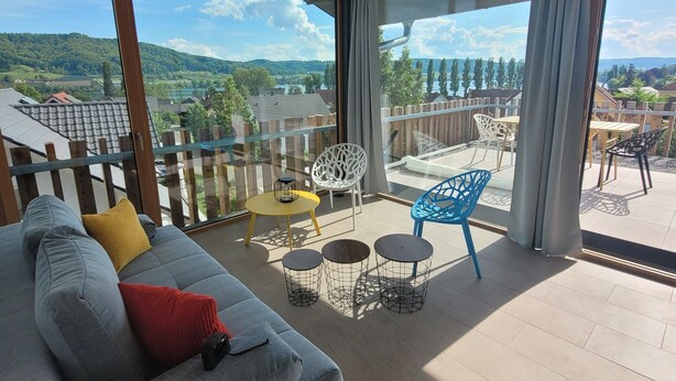 A modern living room with a grey sofa, a yellow table, and a balcony with a view of the countryside. - Exclusive 5-room maisonette architect's house with panoramic lake view and penthouse roof terrace (Öhningen)