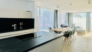 A modern kitchen with a central island, dining area with chairs, and large windows. - Exclusive 5-room maisonette architect's house with panoramic lake view and penthouse roof terrace (Öhningen)