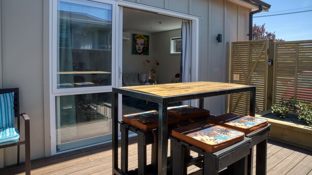 An outdoor patio with a wooden table and chairs, a sliding glass door, and a view of the interior. - Classy Modern Unit.  Walk to shops, bars & cafes.  Pet-Friendly! Bus at gate. (Christchurch)