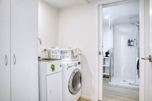 Une petite buanderie équipée d’un lave-linge à chargement frontal, d’un étendoir et d’une cabine de douche en verre.