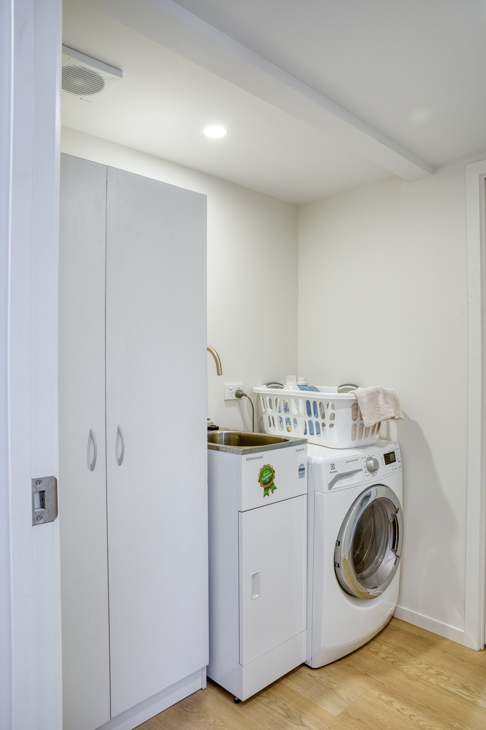 Een praktische wasruimte met een wasmachine en droger, een witte inbouwkast en een klein aanrecht met een wastafel.