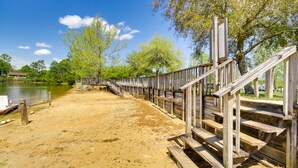 A wooden staircase leading to a sandy area near a body of water, surrounded by trees. - Biloxi Resort Cottage w/ Pool & Lake Access! (Biloxi)
