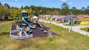 A playground with a slide and climbing structures, surrounded by a white fence. - Biloxi Resort Cottage w/ Pool & Lake Access! (Biloxi)