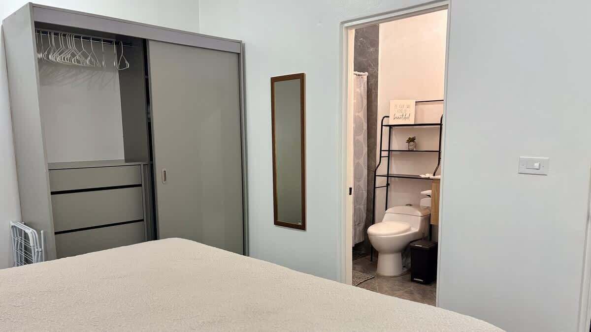 Une chambre à coucher avec un lit, une armoire et une salle de bain visible à travers une porte ouverte.