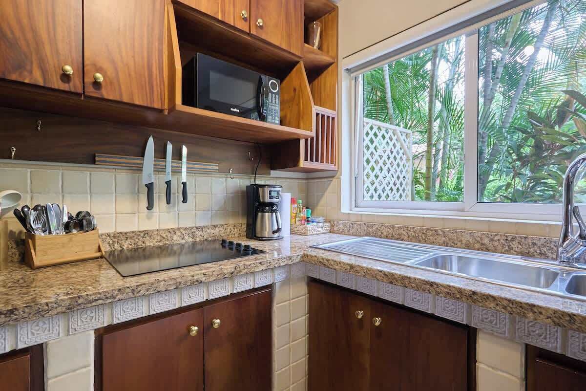 Una cocina con armarios de madera, encimera de granito, microondas, cafetera y ventana con vistas al verdor.