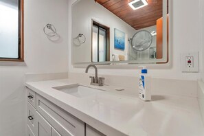 Un bagno con lavandino bianco, uno specchio, un porta asciugamani e una bottiglia di sapone liquido.