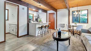 Una cocina moderna con gabinetes blancos y una isla central, un área de comedor con mesa y sillas, y un espacio de sala acogedor con sofá y una mesita de centro.