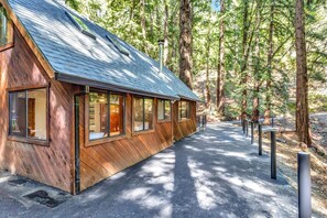 Una baita di legno con ampie finestre, immersa tra alberi alti e un vialetto lastricato.