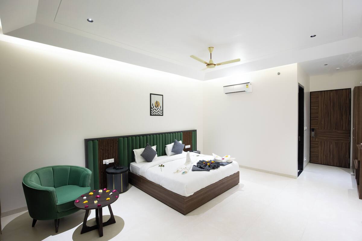 A modern bedroom with a bed, a green armchair, a small table with flowers, and a ceiling fan.