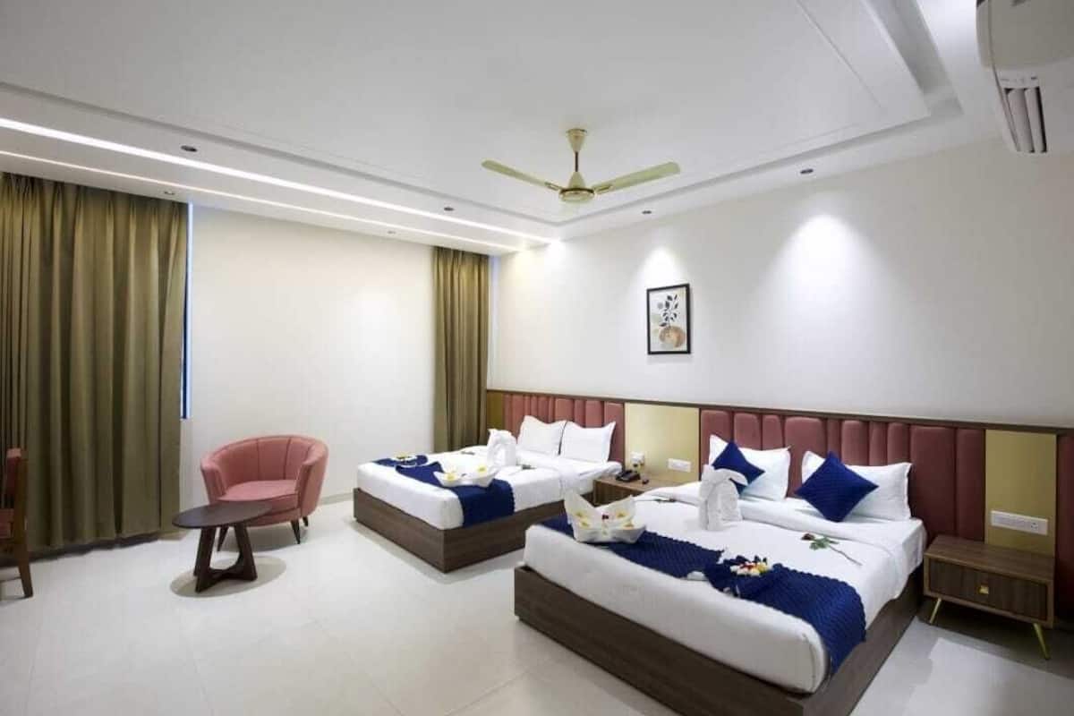 A hotel room with two beds, a chair, a bedside table, and a ceiling fan.