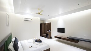 Un dormitorio moderno con cama, ventilador de techo, aire acondicionado, televisor y un banco empotrado.
