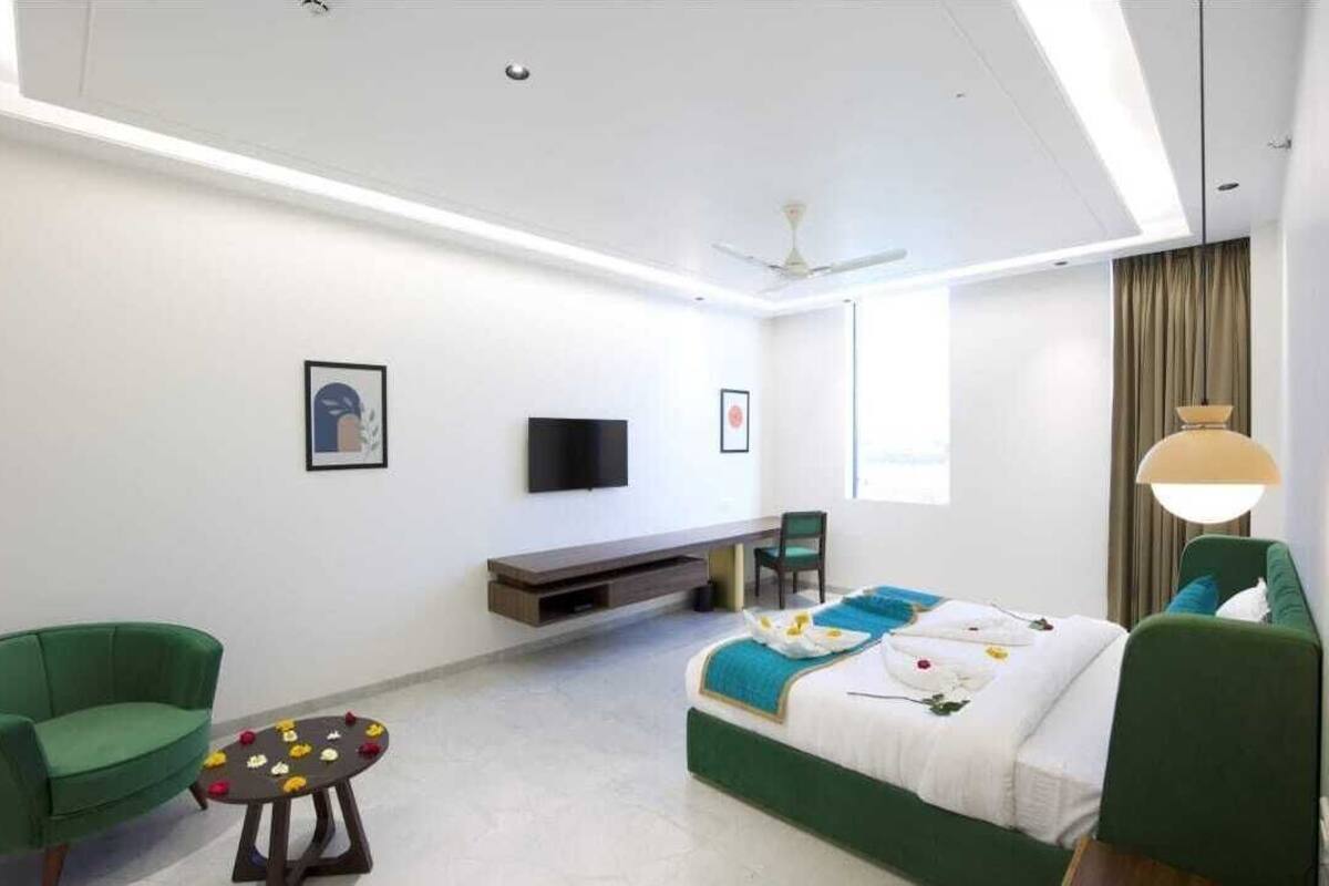 A modern hotel room with a bed, green chairs, a TV, and a ceiling fan.