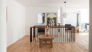 Een moderne woonkamer met een houten vloer, een houten tafel met een bloemenvaas, een zwart metalen hekwerk en een groot abstract schilderij aan de muur.