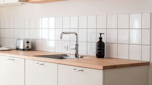 Een keuken met witte tegels, een roestvrijstalen spoelbak, een broodrooster en een plank met bekers en glazen.