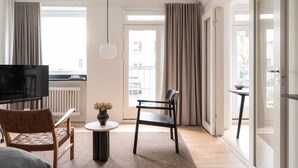 A modern living room with a flat-screen TV, a wicker chair, a small round table with a vase, and a black chair.