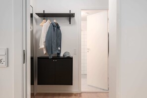 A hallway with a black wardrobe, a coat rack with clothes, and a door leading to a bathroom.
