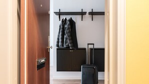 Een kamer met een houten deur, een zwarte koffer en een kapstok met twee jassen.