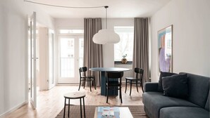 Een moderne woonkamer met een donkergrijze bank, een ronde eettafel met vier stoelen en een hanglamp.