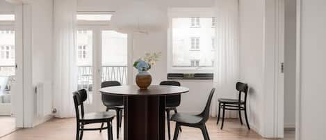 Un comedor con una mesa redonda, sillas negras, un jarrón con flores y una lámpara colgante.