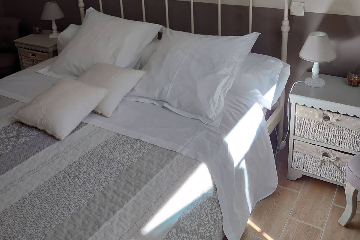 A neatly made bed with white linens and pillows, a bedside table with a lamp, and a wall-mounted artwork with the word "LOVE".