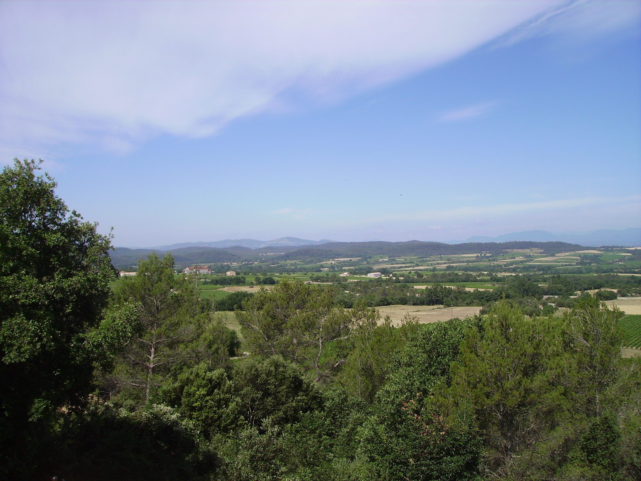 Un panorama sur un paysage rural, avec des collines ondoyantes, des bâtiments dispersés et de vastes forêts.