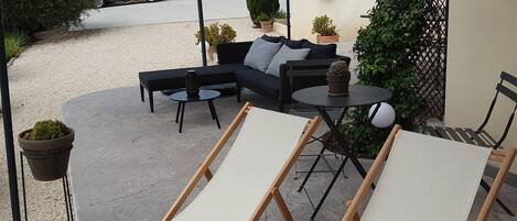 Un espace extérieur aménagé avec un coin salon couvert, comprenant un canapé et deux fauteuils, une table et une plante en pot.