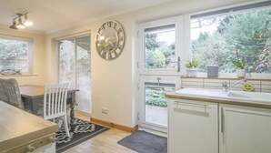 A kitchen with a clock, a dining table, and a window with a view of greenery.