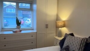 A bedroom with a bed, a window with blinds, a potted plant, a lamp, and a wardrobe.