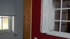 Un baño con un inodoro blanco, una ventana con persianas y una pared roja.