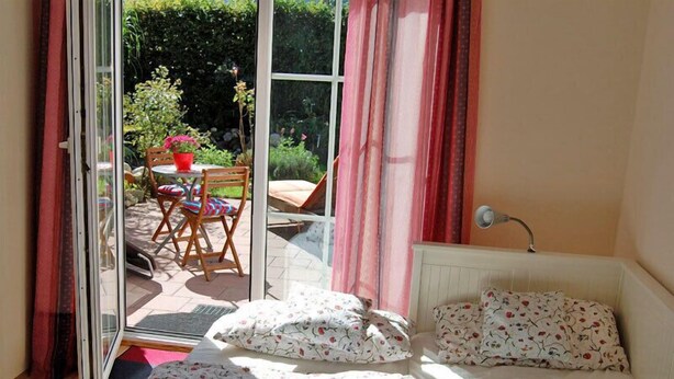 Un dormitorio con cama, mesita de noche, ventana y vistas a un patio exterior con mesa y sillas.