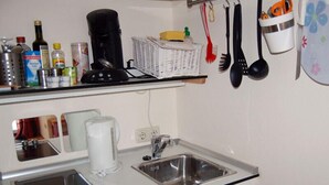 Una cocina compacta con un lavamanos, una cafetera y diversos utensilios de cocina sobre la encimera.