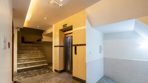 A modern hotel lobby with a marble staircase, an elevator, and a sign indicating the first floor. - Hotel Stay House Inn (New Delhi)