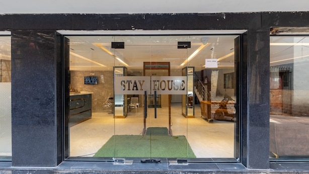 A hotel entrance with a 'STAY HOUSE' sign, a reception desk, and a staircase leading inside. - Hotel Stay House Inn (New Delhi)