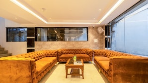 A modern living room with a sectional sofa, a coffee table, and large windows offering views of the outside. - Hotel Stay House Inn (New Delhi)