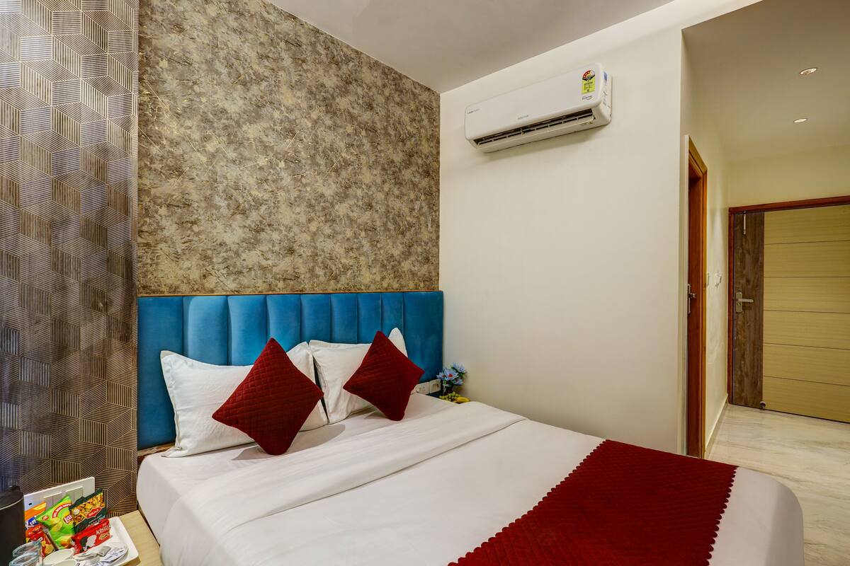 A hotel room with a blue headboard, white bedding, and a red throw blanket.