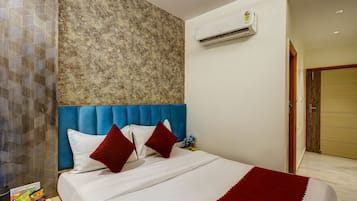 A hotel room with a blue headboard, white bedding, and a red throw blanket.