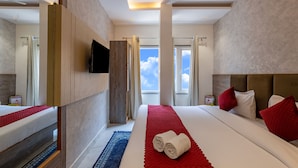 A hotel room with a large bed, a TV, a ceiling fan, and a view of the sky. - Hotel Stay House Inn (New Delhi)